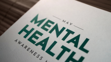 "Mental Health Awareness" in black and green ink typed out on a piece of printer paper sitting on a wood desk